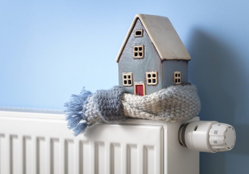 House model wrapped in scarf on radiator home winter heating and insulation background fuel and energy crisis concept
